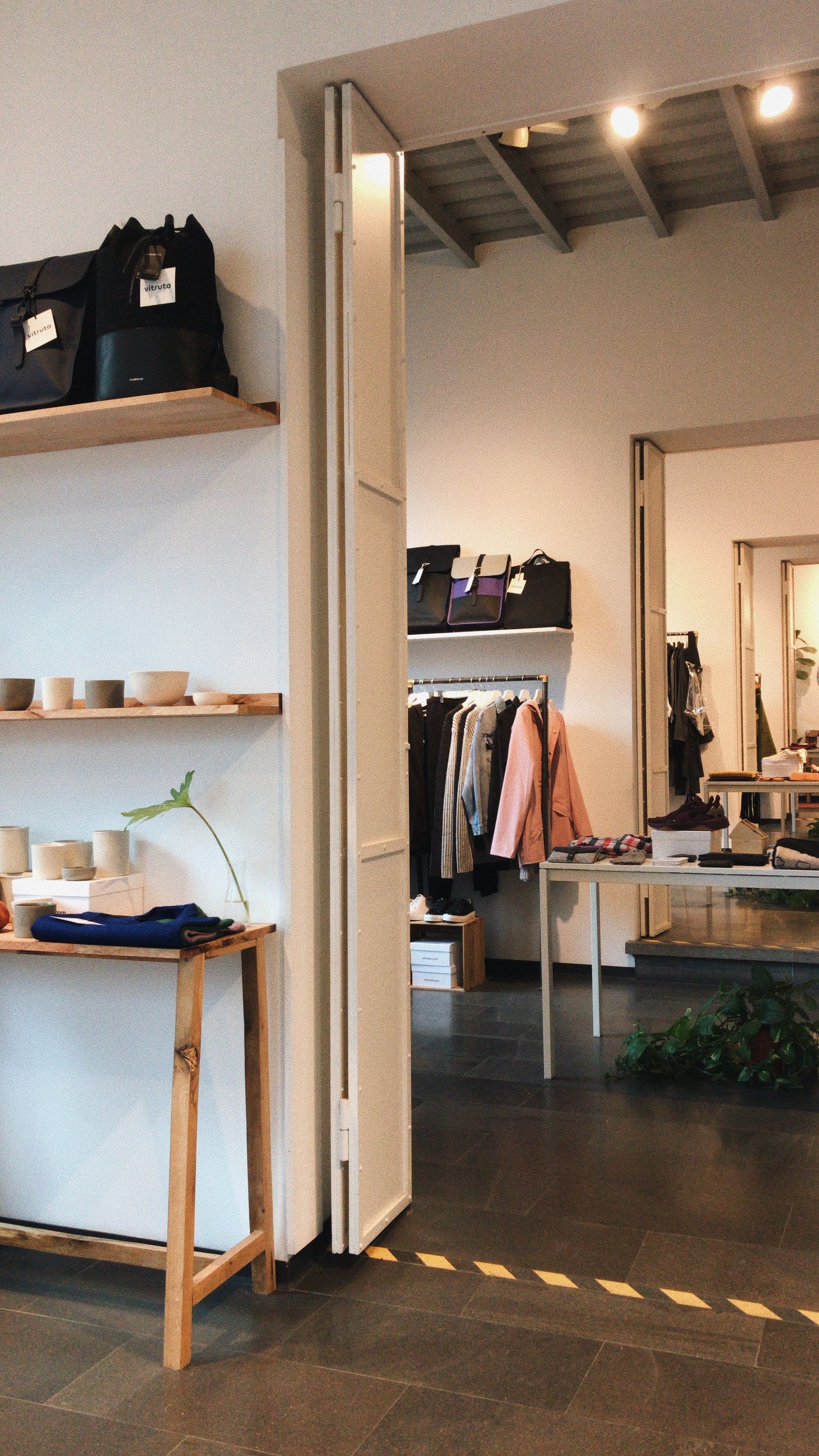 Boutique interior with clothing rails, open display shelves and a sequence of connected rooms.
